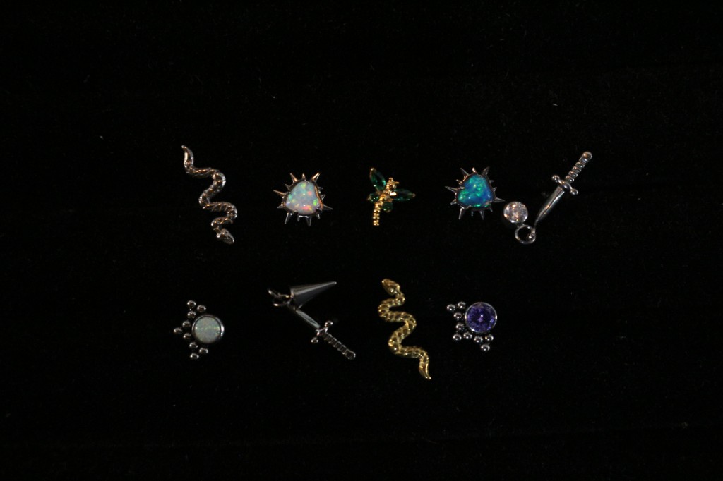 Piercings d'autor amb opal, serpents i espases sobre fons negre